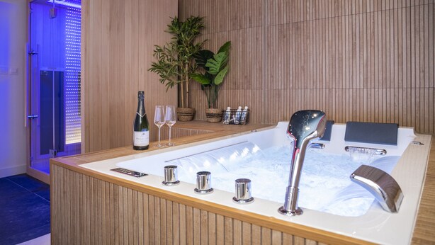 A modern bathroom with a wooden vanity, a large bathtub, and a potted plant.