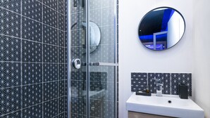 A modern bathroom with a geometric tile backsplash, a round mirror, and a white sink with a wooden cabinet.