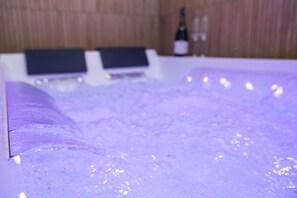 A bathtub with water jets, a bottle of wine, and a remote control on a wooden wall. - Art Deco Champagne & Spa (Reims)