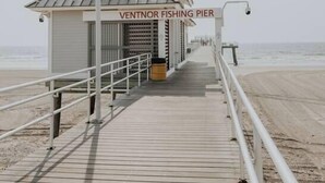 Une promenade en bois mène à un petit bâtiment portant l’inscription « VENTNOR FISHING PIER », avec une rambarde en métal et une poubelle.