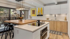 Een moderne keuken met een centraal eiland, een ingebouwde oven en een groot raam met uitzicht op een terras.