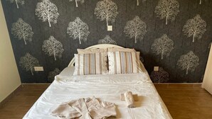 Un lit bien fait, avec des oreillers à rayures et une couverture pliée, devant un mur recouvert d’un papier peint à motifs d’arbres.