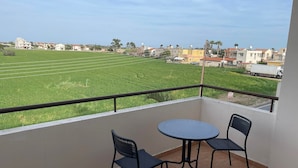 Un balcon avec deux chaises et une table, donnant sur un champ verdoyant et des immeubles d’habitation.