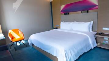 A hotel room with a large bed, a modern orange chair, and a decorative wall piece.