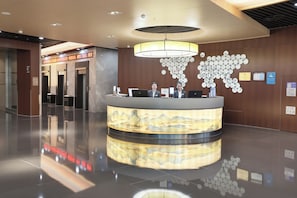 Un mostrador de recepción de hotel con una pantalla digital, una obra de arte en la pared e iluminación empotrada en el techo.