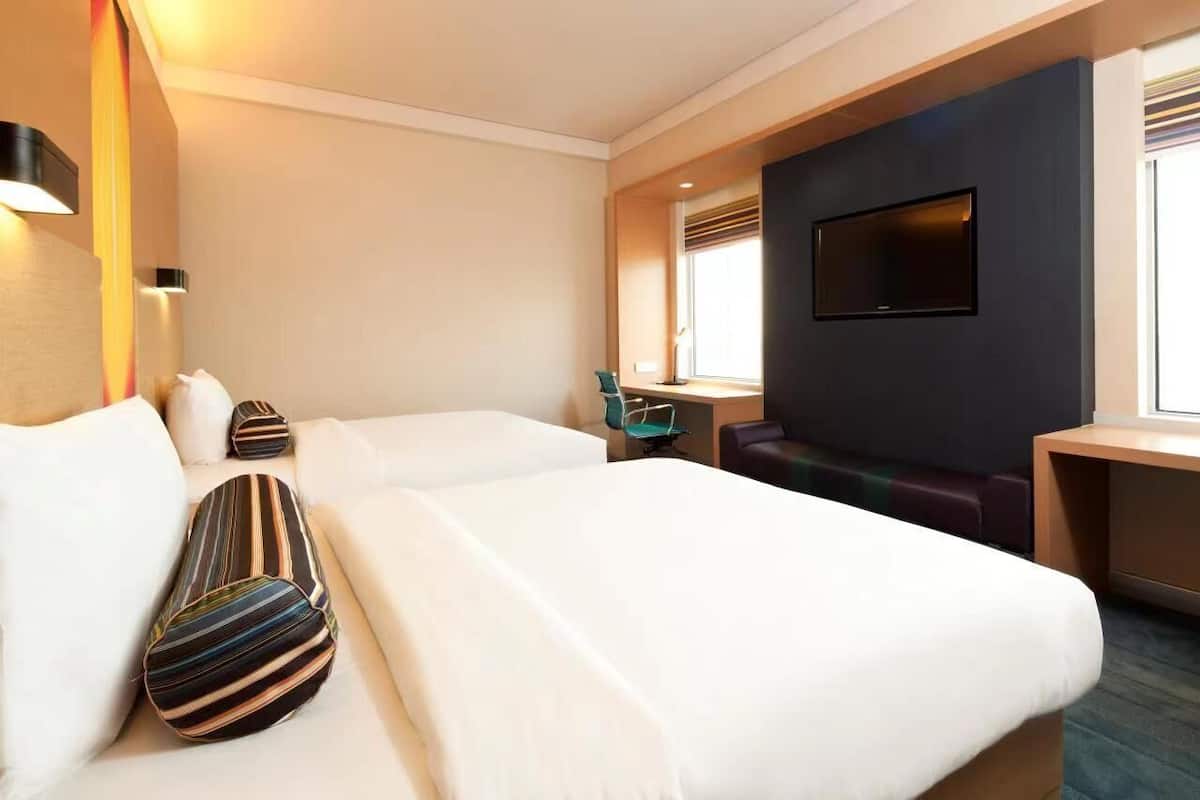A hotel room with two beds, a TV, a desk, and a window.