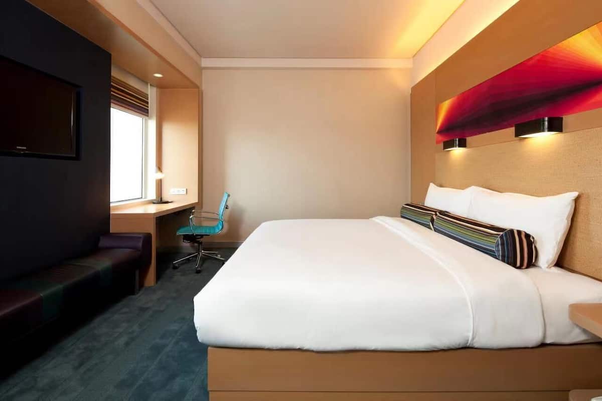 A hotel room with a large bed, a desk, a chair, and a TV mounted on the wall.