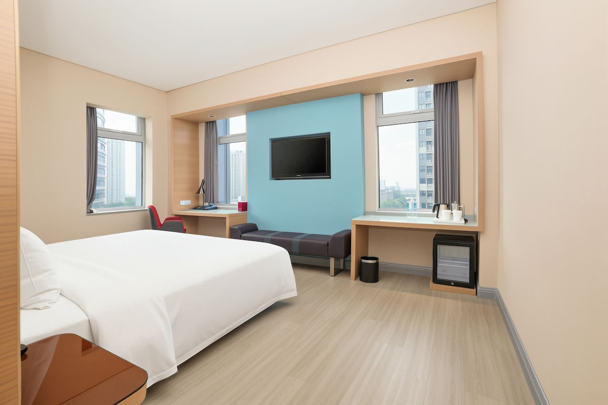 A hotel room with a bed, desk, chair, TV, and a heater.