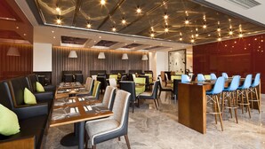 Un hall d’hôtel moderne doté de plusieurs espaces de détente, notamment un bar et des tables à manger.