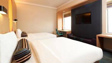 A hotel room with two beds, a TV, a desk, and a window.