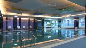 Une piscine intérieure moderne, dotée de chaises longues et d’un design de plafond original.