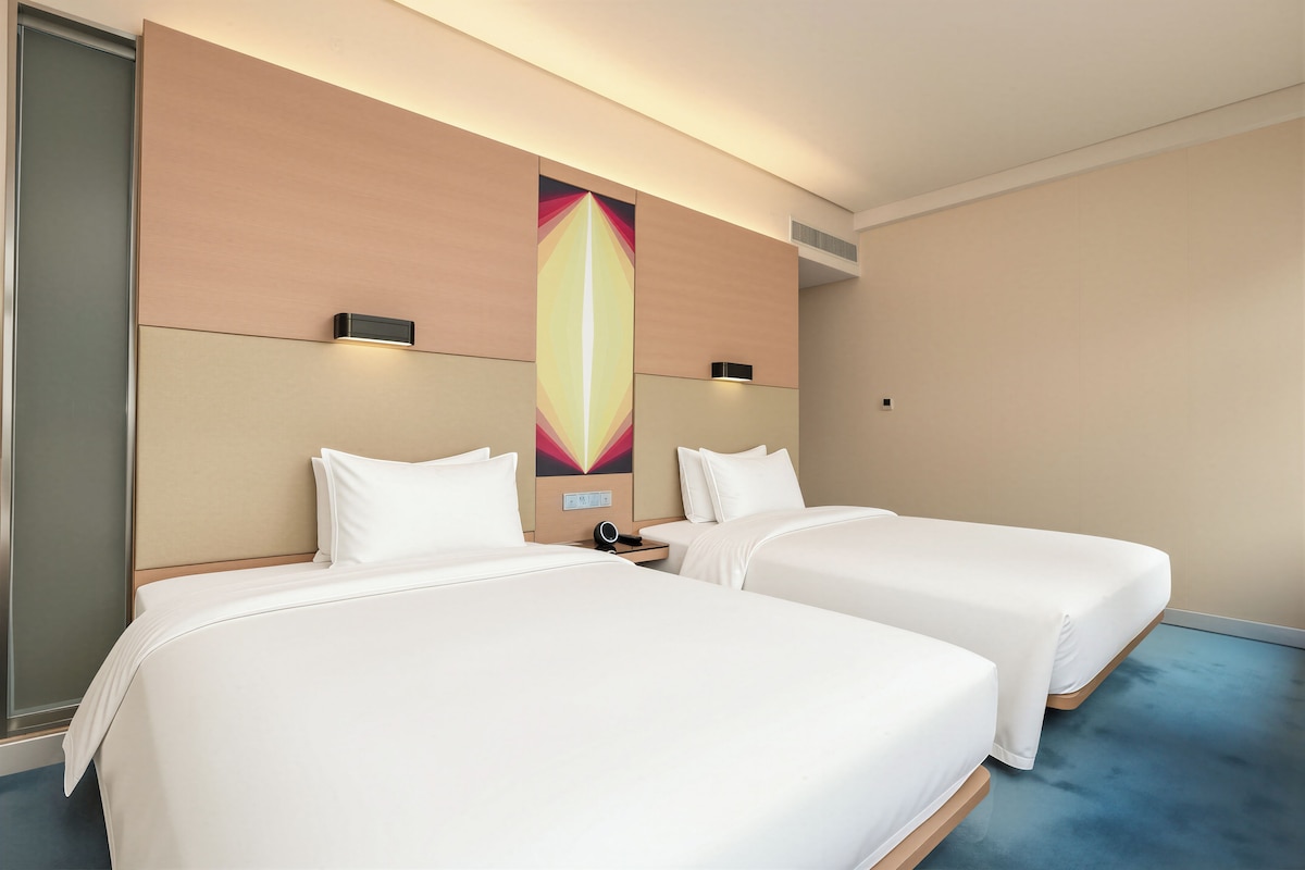 A hotel room with two beds, a large wall art piece, and a modern design.