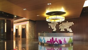 Un hall d’entrée moderne avec un sol réfléchissant, un comptoir d’accueil central orné d’un motif coloré représentant un paysage urbain, et un luminaire au plafond au design original.