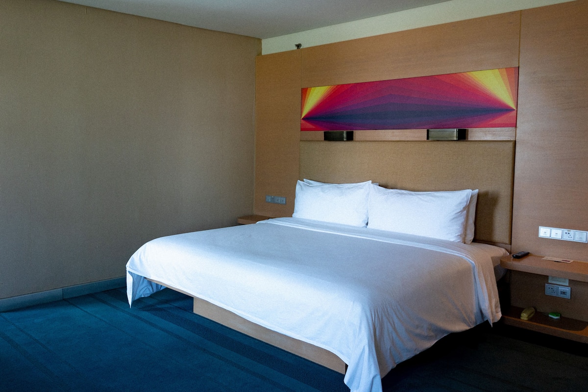 A hotel room with a bed, a nightstand, a wall-mounted TV, and a power outlet.