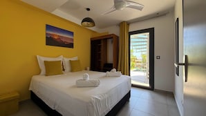 A hotel room with a bed, a painting, a ceiling fan, and a view of a building through a glass door. - Belle Villa Avec Piscine à 200m de la Plage ! (Saint-Leu)