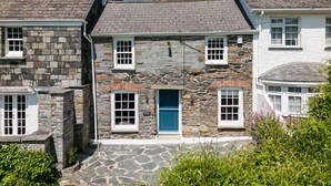 Ein Steinhaus mit einer blauen Tür, mehreren Fenstern und einer Steintreppe, die zum Eingang führt.