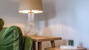 Ein grünes Sofa, ein Holztisch mit einer Lampe und ein kleiner Holztisch mit einem Buch und einer grünen Tasse.