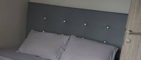 A neatly made bed with a grey headboard and white bedding.