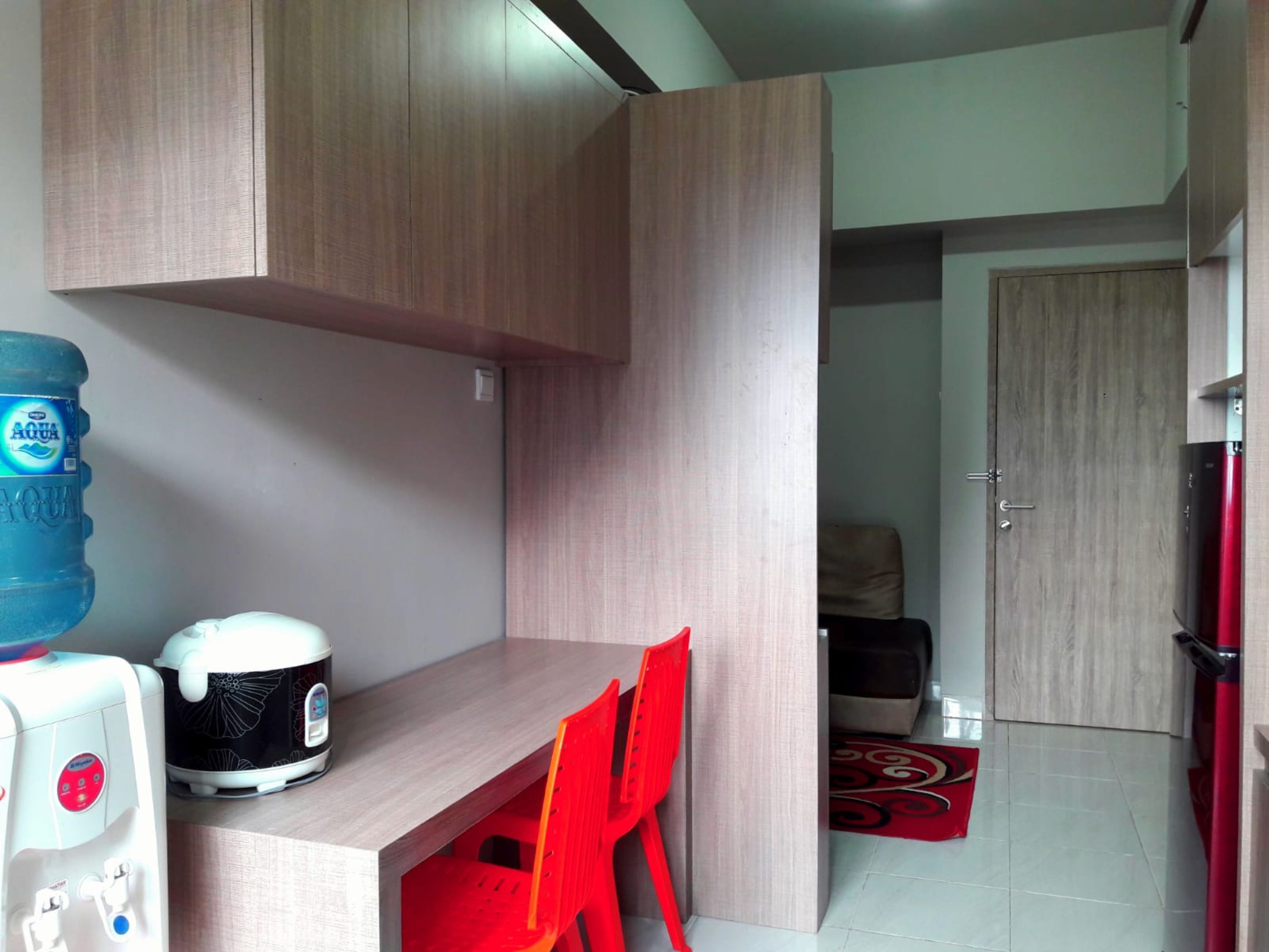 A compact kitchen with a countertop, a water dispenser, a rice cooker, and a red chair.