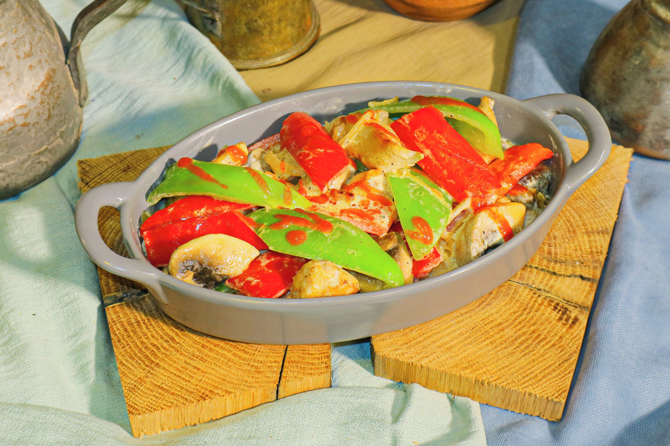 A dish of food in a ceramic dish on a wooden table with a cloth napkin underneath.
