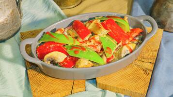 A dish of food in a ceramic dish on a wooden table with a cloth napkin underneath.