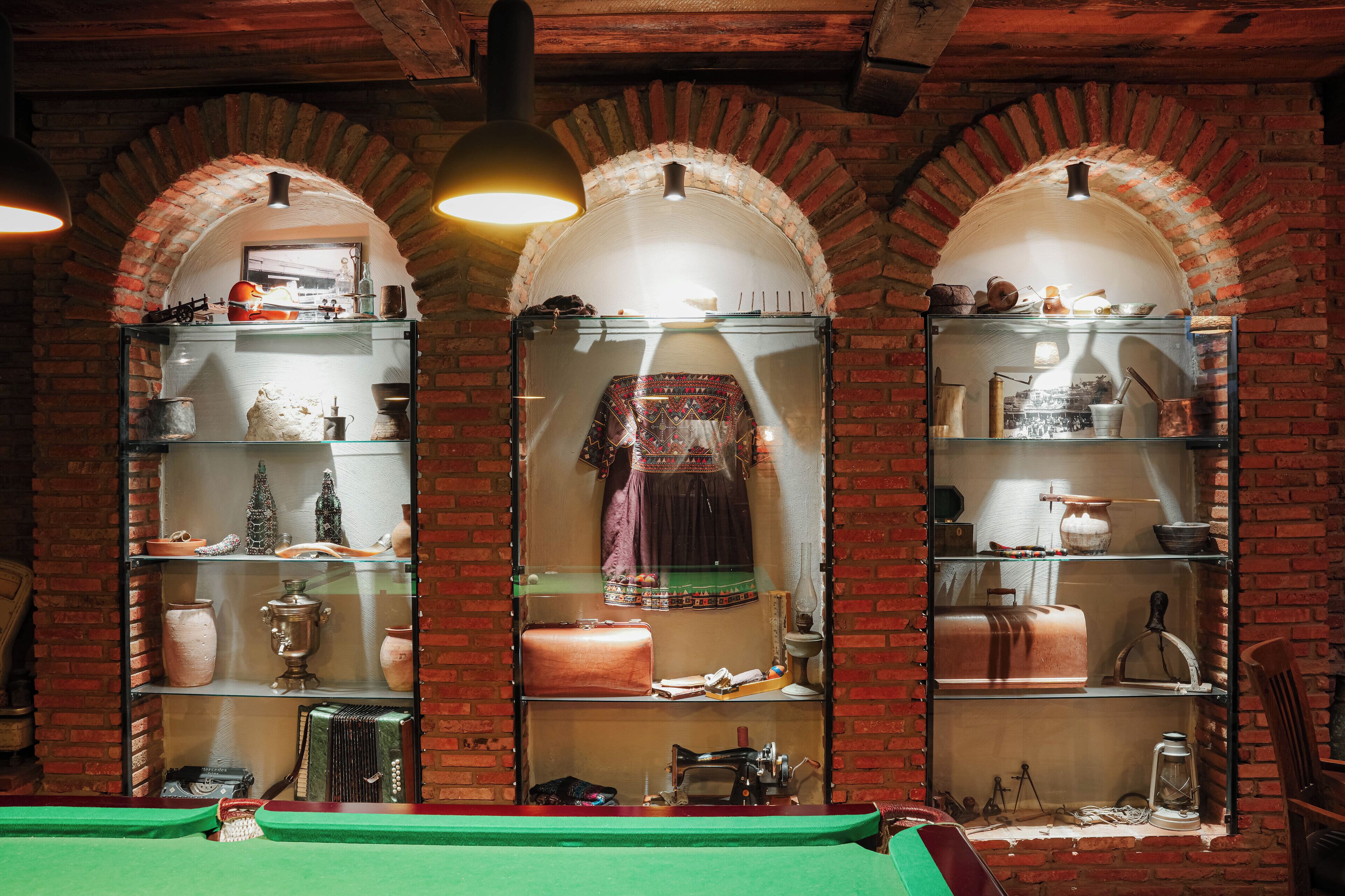 A room with arched brick walls, shelves displaying various items, and a billiards table.
