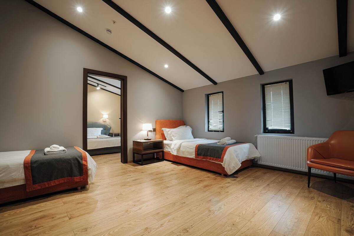 Una habitación de hotel con dos camas, una zona de estar, un espejo y un televisor.