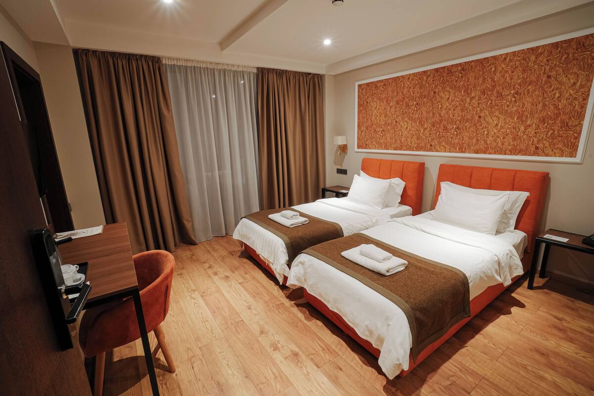 Habitación de hotel con dos camas, un escritorio, una silla y un ventanal con cortinas.