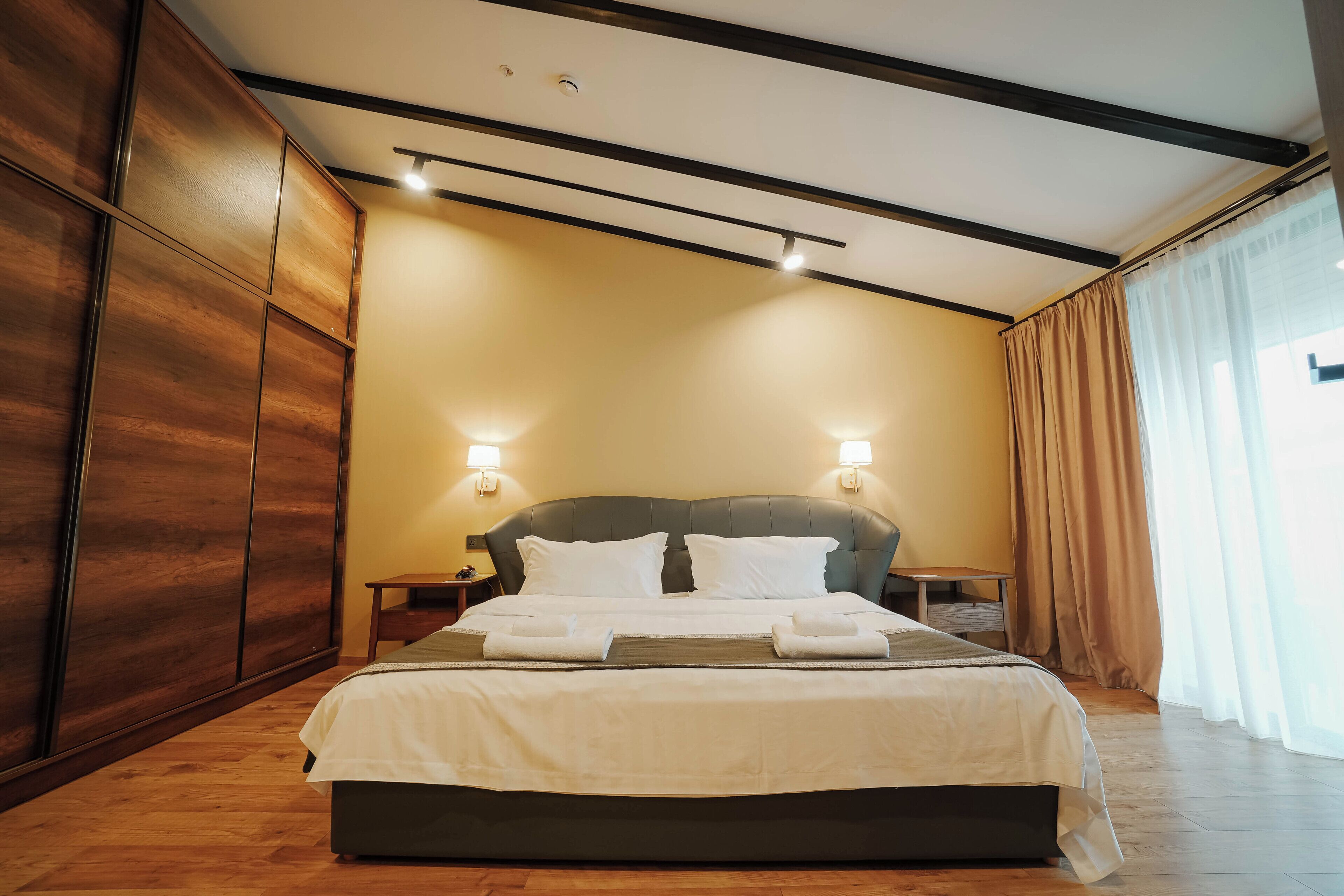 A modern hotel room with a large bed, wooden wardrobe, and two bedside lamps.
