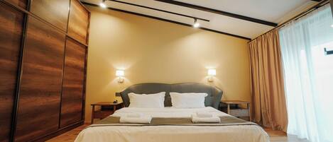 A modern hotel room with a large bed, wooden wardrobe, and two bedside lamps.