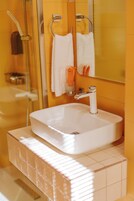 Un baño con un lavabo blanco, cabina de ducha de cristal y un espejo sobre el lavabo.