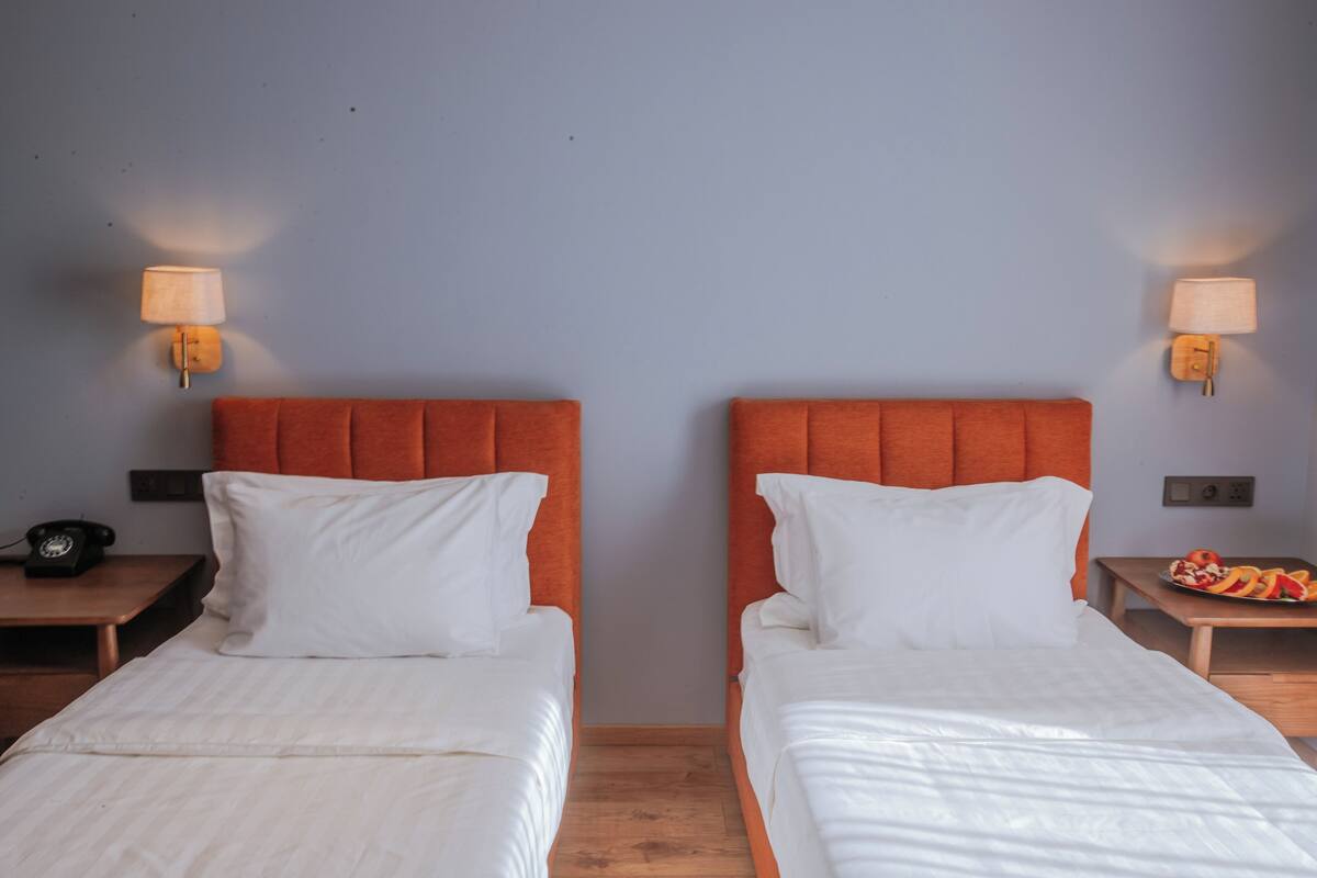 Dos camas individuales con cabeceros naranja, ropa de cama blanca y lámparas de noche.