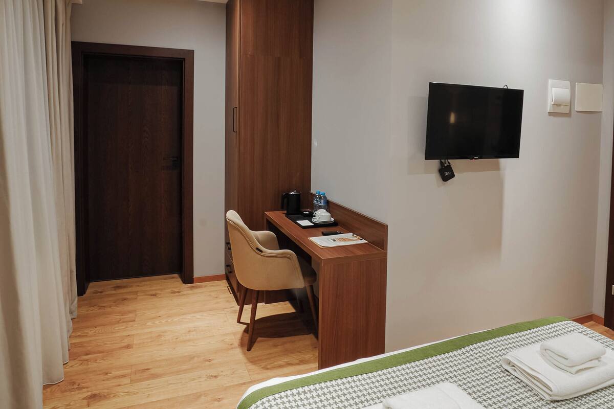 Habitación de hotel con cama, escritorio, silla, televisor y puerta de madera.