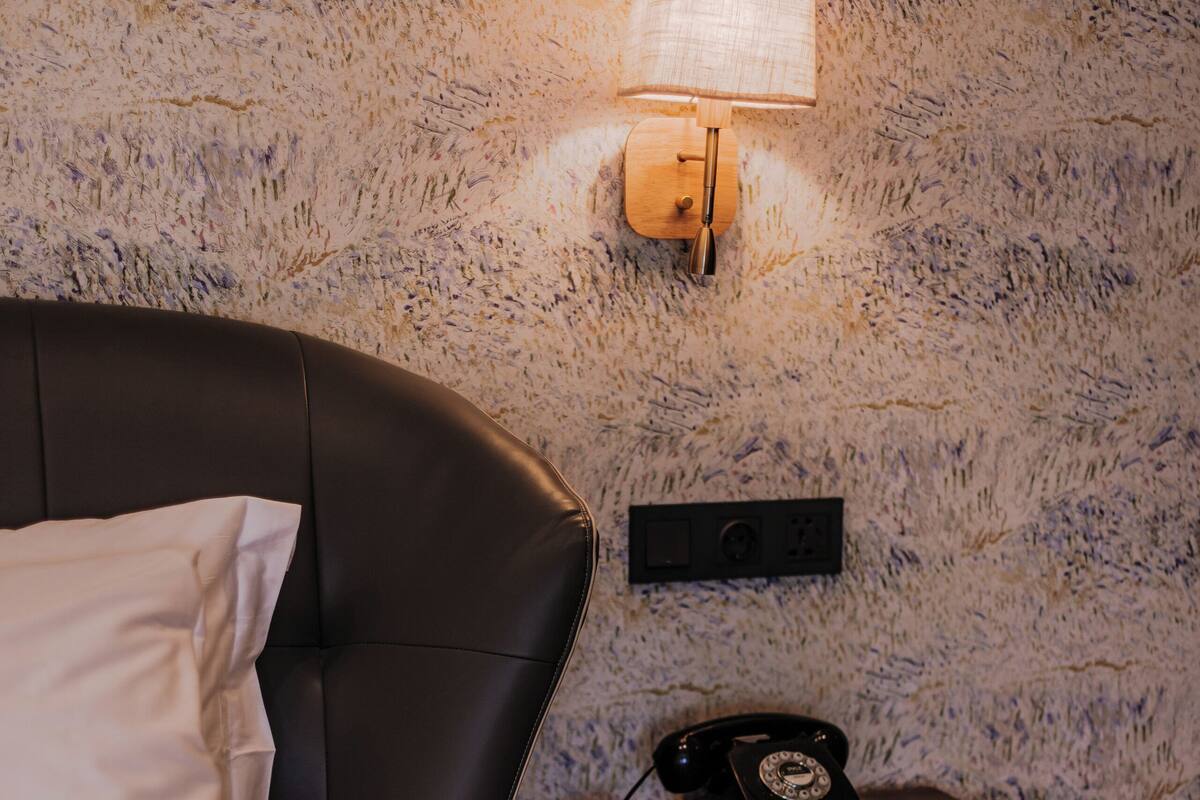 Un dormitorio con cama, mesita de noche, teléfono y lámpara de pared.