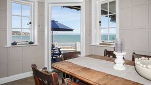 Een eethoek met een tafel, stoelen en uitzicht op de oceaan door open ramen.
