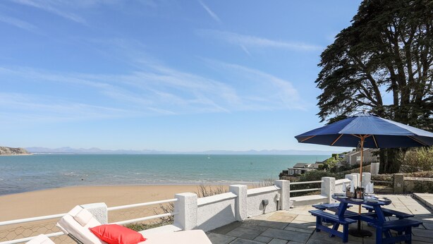 Een terras aan het strand met lounge stoelen en een tafel onder een blauwe parasol, met uitzicht op de zee.