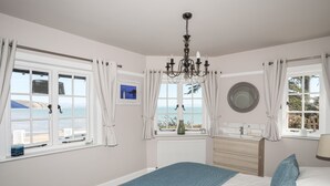 Een slaapkamer met een bed, een kroonluchter, uitzicht op zee en een raam met gordijnen.