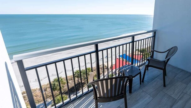 Un balcon avec vue sur l’océan, deux chaises et une table.
