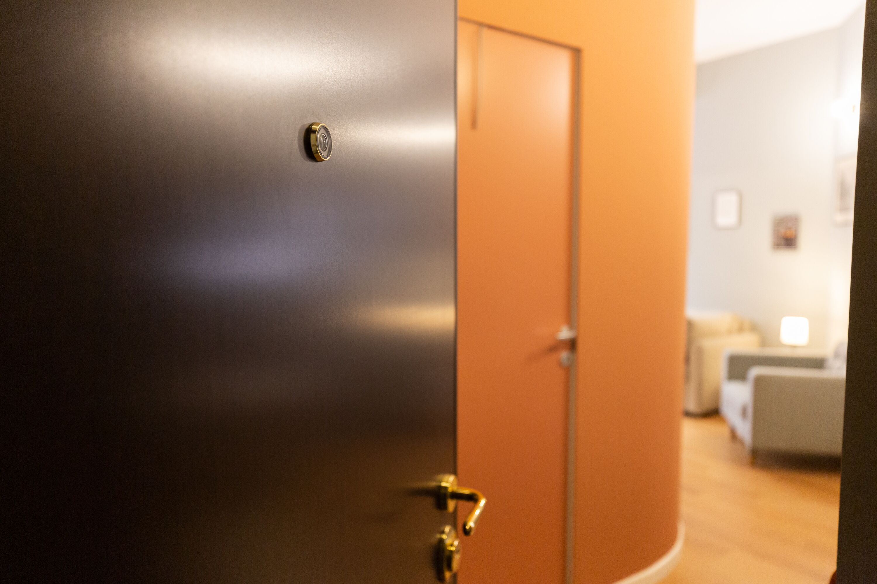 A closed door with a brass handle and a keyhole, leading to a room with a wooden floor and a white couch.