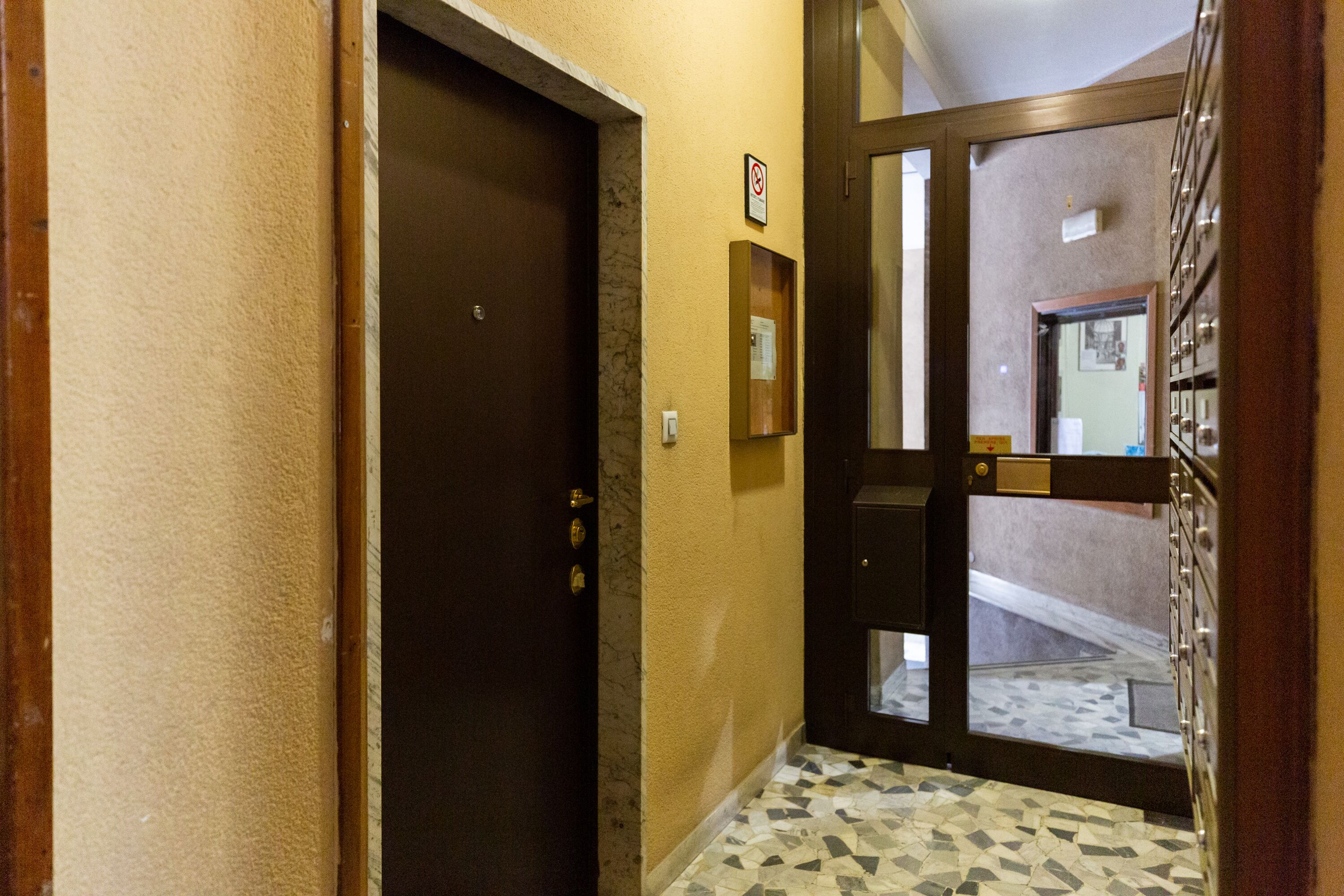 A hallway with a brown door, a no-smoking sign, a small framed picture, and a tiled floor.