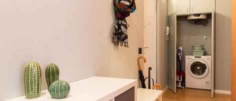 Una habitación pequeña y limpia con una mesa blanca, una lavadora y un tendedero.