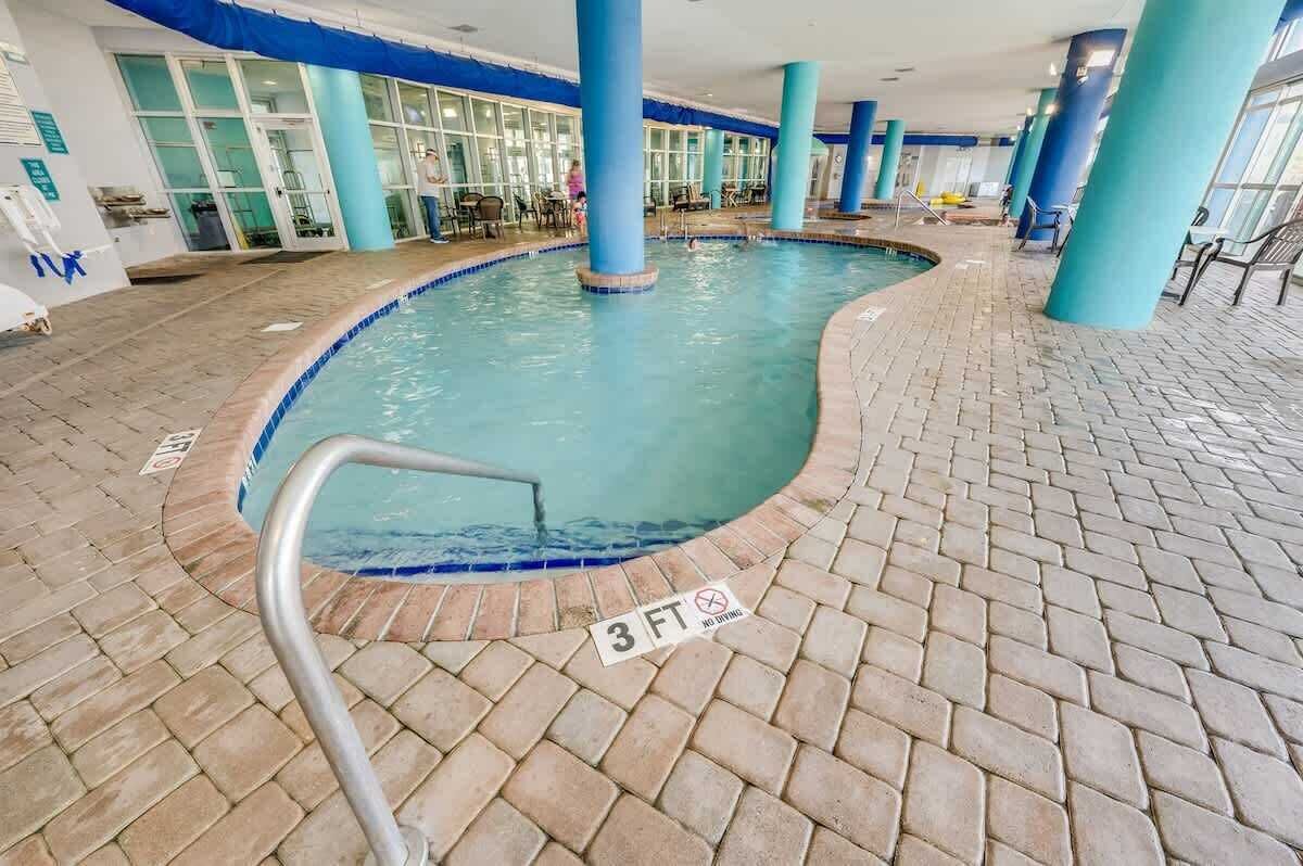 En indendørs swimmingpool med et skilt, der angiver en dybde på 3 fod, omgivet af blå søjler og flisegulv.