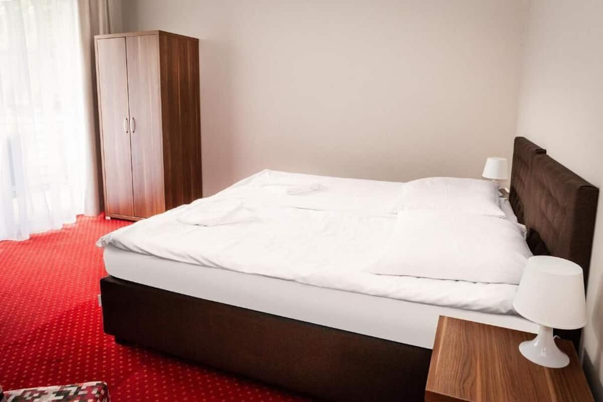 A neatly made bed with white linens, a wooden headboard, and a bedside table with a lamp.