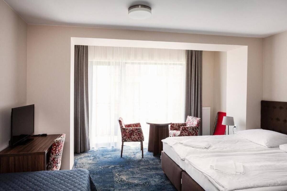 A hotel room with a bed, a desk, a chair, a small table, and a television.