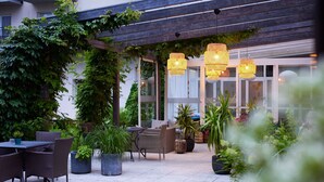 Um pátio externo com móveis de vime, plantas em vasos e luzes penduradas.