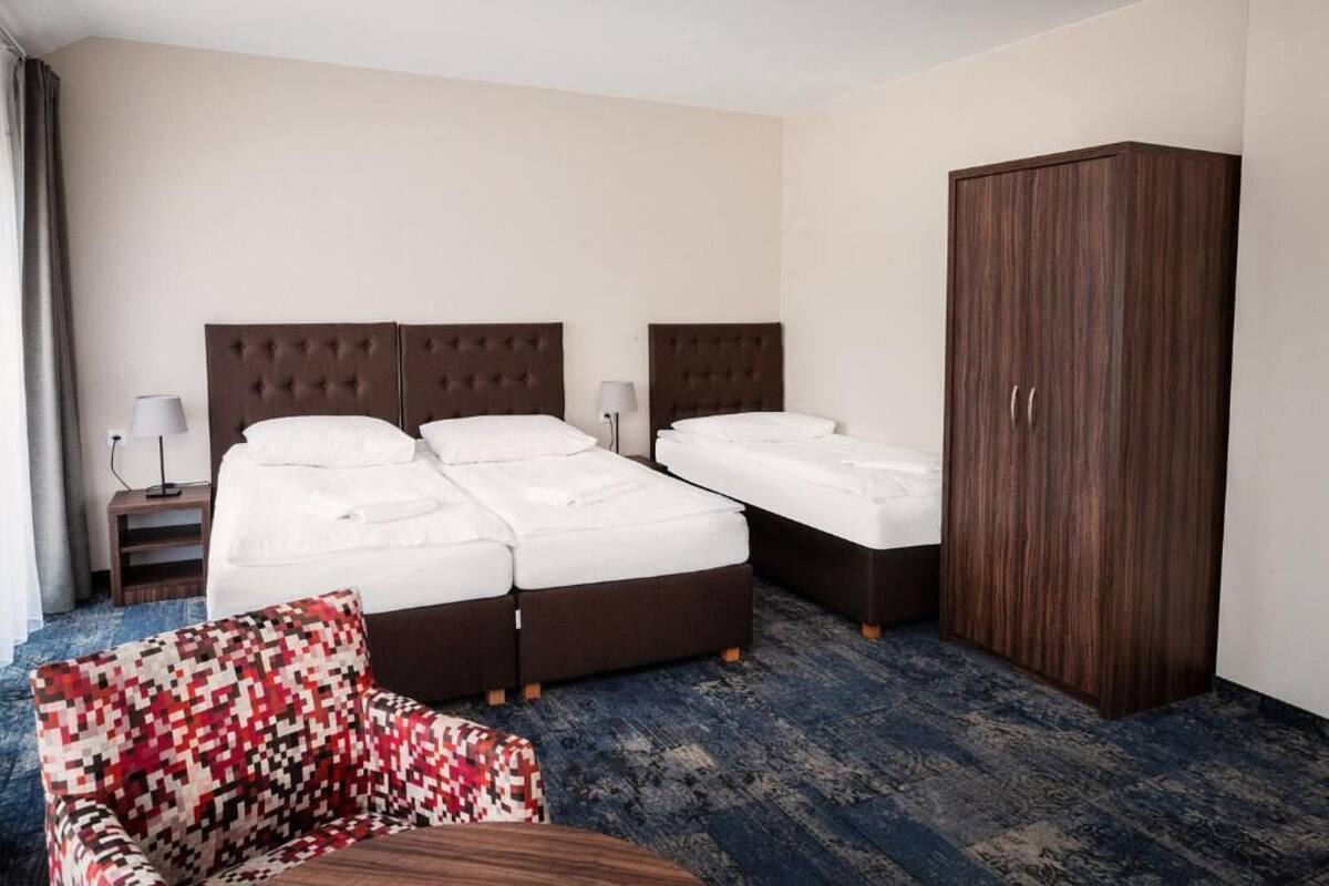A hotel room with two beds, a wardrobe, a chair, and a small table.