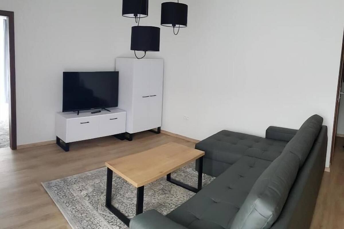 A modern living room with a grey sofa, a wooden coffee table, a TV on a white cabinet, and two black pendant lights.