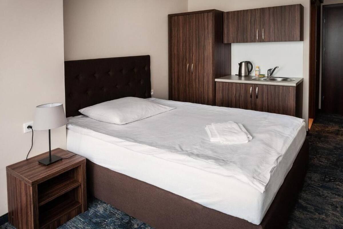 A hotel room with a bed, a nightstand, a desk with a sink, and a wardrobe.