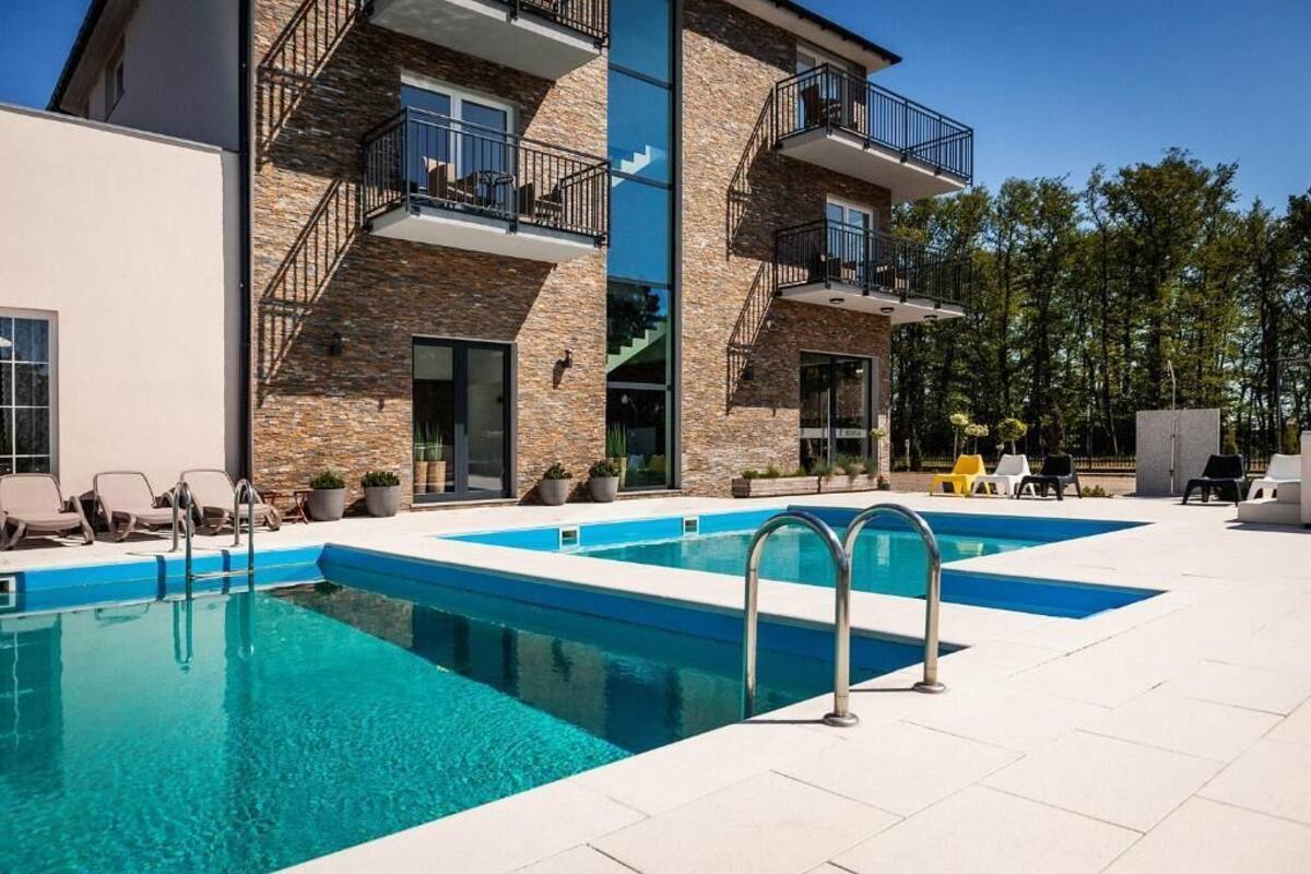 A modern building with a swimming pool, outdoor seating, and a stone facade.