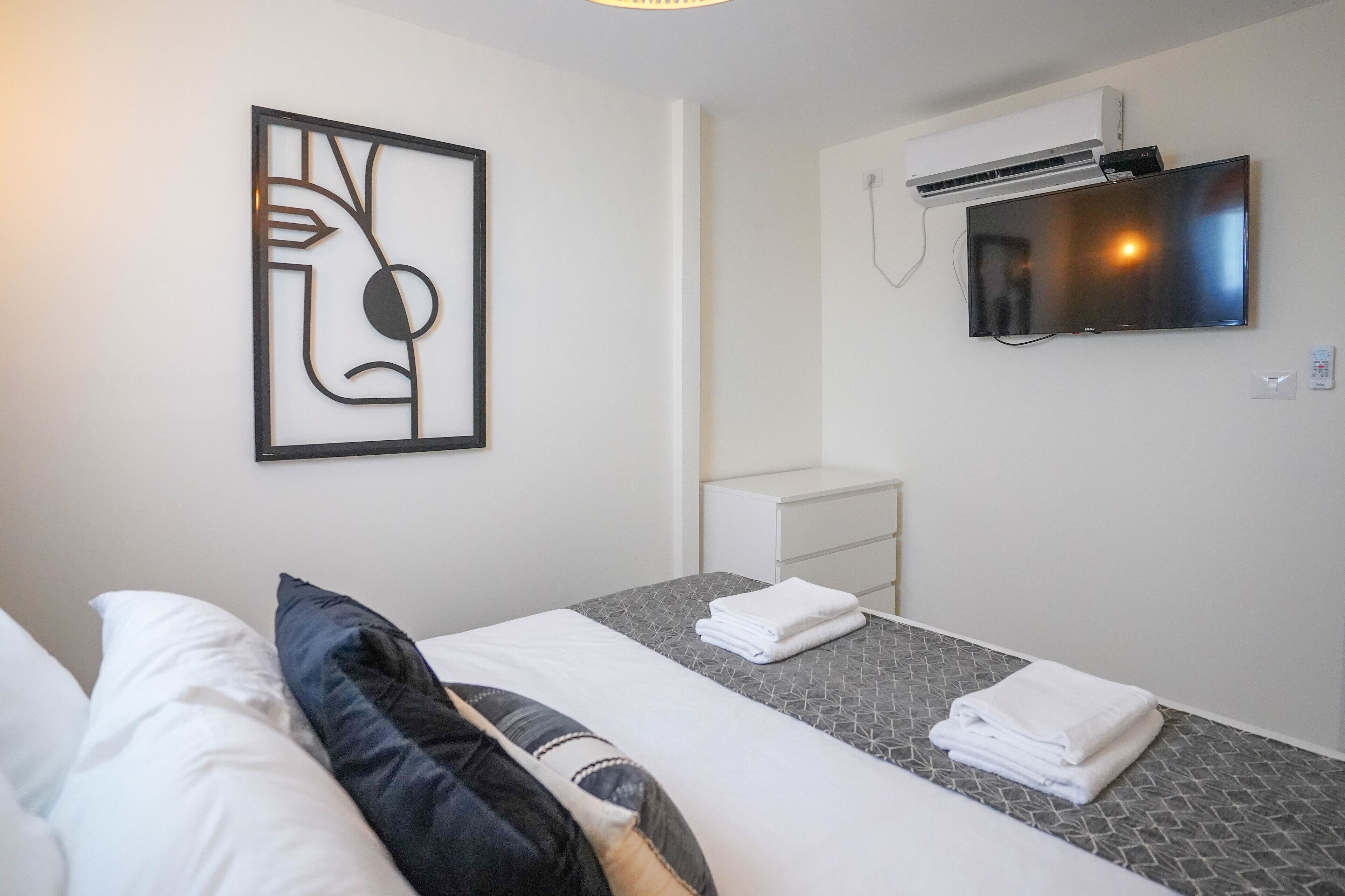 Een hotelkamer met een bed, een nachtkastje, een aan de muur bevestigde televisie en een airconditioning.
